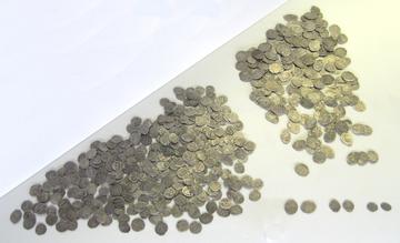 Две горки мелких серебряных монет неправильной овальной формы на светлом фоне