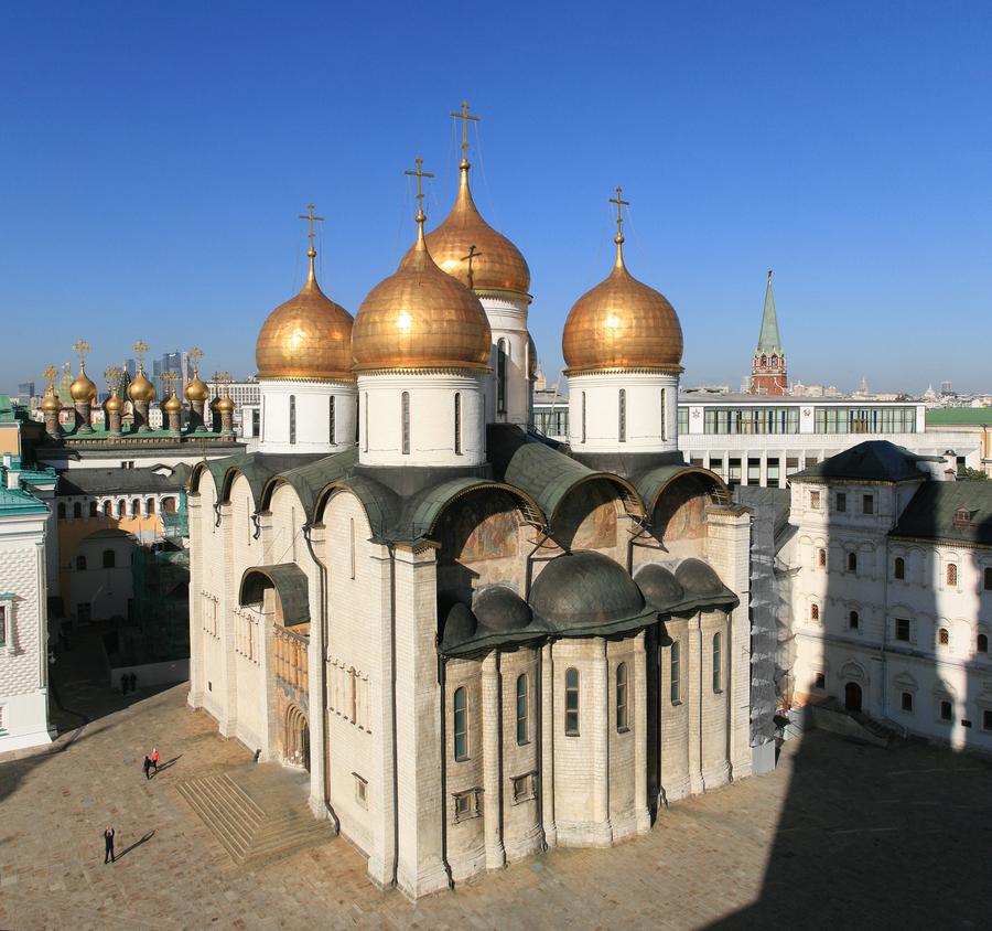 Белый храм с пятью золотыми главами и полукруглыми завершениями стен стоит на мощёной площади, вокруг него другие кремлёвские здания