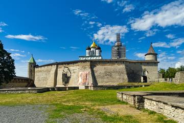 Длинная серая каменная крепостная стена с башнями под высокими шатровыми крышами, над стеной видны золотой купол собора и высокая колокольня, перед стеной зелёная лужайка