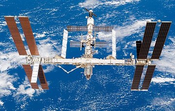 Международная космическая станция с солнечными батареями на фоне голубой Земли с облаками