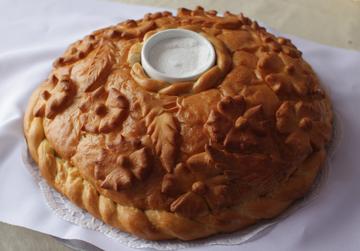 Круглый румяный каравай с лепным узором, в середине — белая солонка с солью