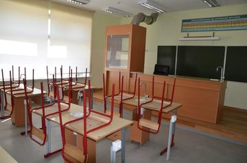 Пустой школьный кабинет: парты со стульями, поднятыми на столешницы, доска, вытяжной шкаф у стены
